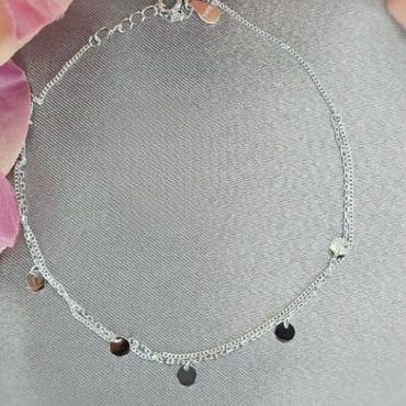 A sterling silver bracelet with a series of round beads and two black discs, displayed on a textured background with flowers.