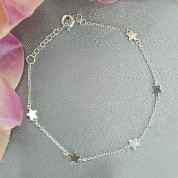 A sterling silver bracelet with star-shaped charms and a small chain, displayed on a surface with pink flower accents.