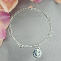 A sterling silver bracelet with a smiley face charm, displayed on a grey background with flower accents.