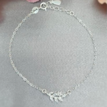 A sterling silver bracelet featuring a single leaf design on a chain, displayed against a floral background.