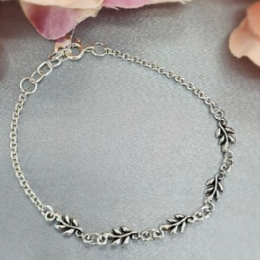 A sterling silver bracelet with a leaf motif, displayed on a surface with pink flower accents.