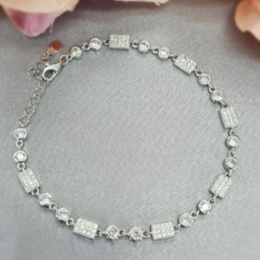 A sterling silver bracelet with pavé cubic zirconia detail, showcased on a surface with a floral background.