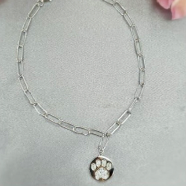 A sterling silver paperclip chain bracelet with a paw disc on a chain of flowers, placed on a surface with cubic zirconia flowers.