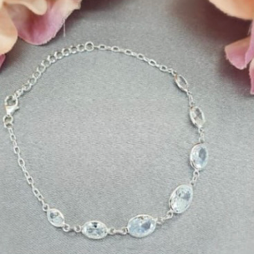 A sterling silver bracelet with clear cubic zirconia stones placed on a surface with pink flower petals around it.