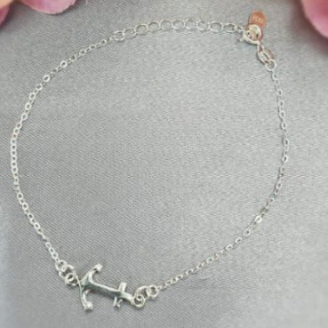 A sterling silver bracelet with an anchor charm, displayed on a surface with a background of pink flowers.