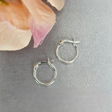 A pair of sterling silver hoop earrings placed on a textured surface with a background of soft floral accents.