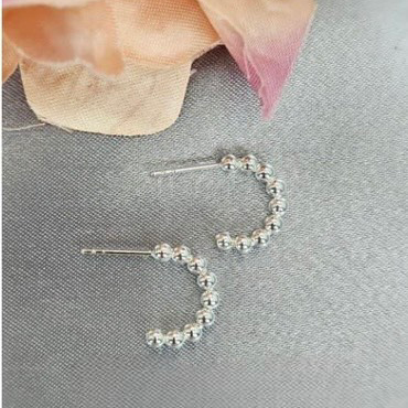 A pair of 3mm sterling silver hoop earrings with a half-circle silhouette and a ball detail, displayed on a grey surface with a flower in the background.