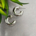 A pair of silver hoop earrings placed on a textured grey fabric surface.