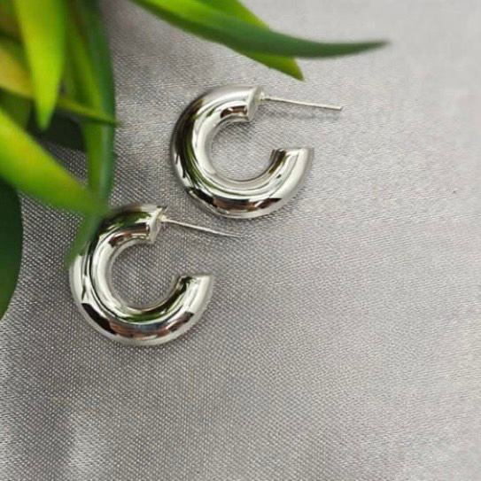 A pair of silver hoop earrings placed on a textured grey fabric surface.