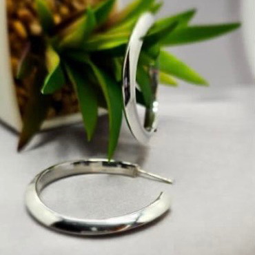 A pair of sterling silver hoop earrings lies on a flat surface with a blurred green plant in the background.