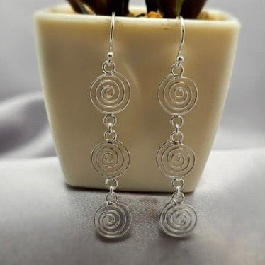 Sterling silver drop earrings displayed on a table with a plant in the background.
