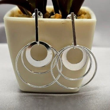 A pair of sterling silver modern three circle earrings displayed in front of a potted plant.