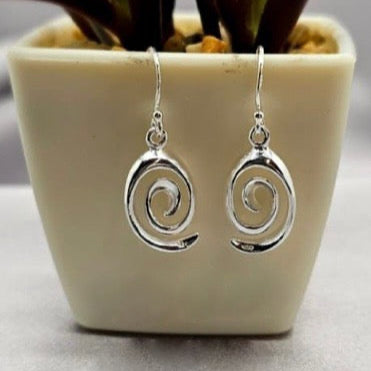 A pair of sterling silver spiral hanging earrings displayed in a white vase with a plant background.