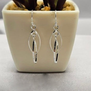 A pair of sterling silver double twist hanging earrings displayed in a white vase with a green plant.