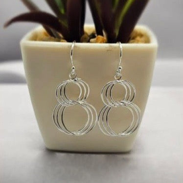 A pair of sterling silver double interlinked ring earrings displayed in front of a potted plant.