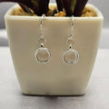 A pair of sterling silver circle drop earrings displayed in a white vase with a plant background.