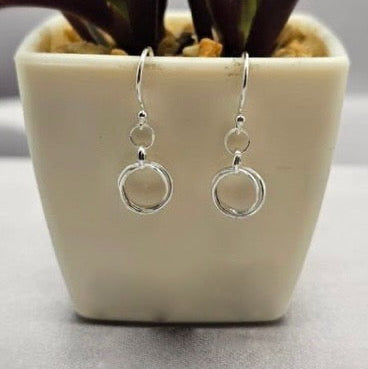 A pair of sterling silver circle drop earrings displayed in a white vase with a plant background.