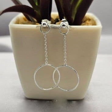 A pair of sterling silver large circle chain drop earrings displayed on a white pot with a green plant.