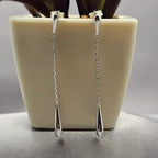 A pair of sterling silver drop earrings hanging from a white plant pot.