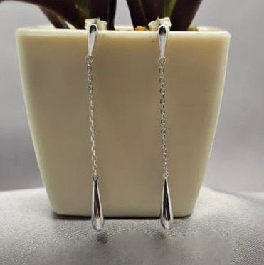 A pair of sterling silver drop earrings hanging from a white plant pot.