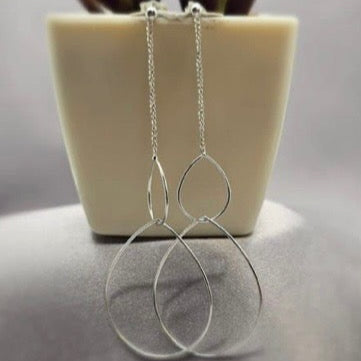 A pair of sterling silver drop earrings with double teardrop hoops displayed on a white stand.