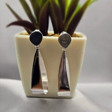 A pair of sterling silver circle drop earrings displayed in a white vase with a green plant.