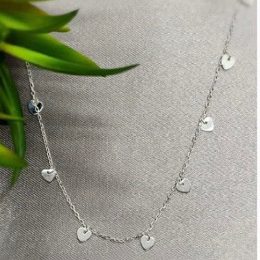 A sterling silver necklace with multiple tiny heart charms displayed against a textured background.