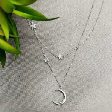 A sterling silver necklace with a moon and stars design, displayed against a textured background with a green plant.