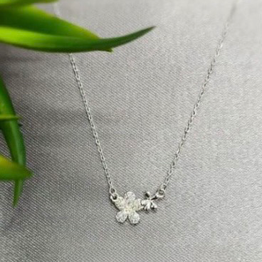 A sterling silver necklace with a double flower pendant, displayed against a textured grey background with a green leaf.