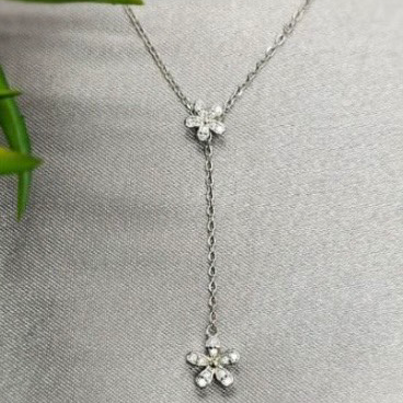 A V-shaped necklace with cubic zirconia detailed flower pendants on a silver chain, displayed against a grey background.