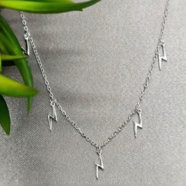 A sterling silver necklace with lightning bolt charms displayed on a mannequin bust with a blurred green background.