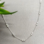 A sterling silver necklace with a square detail lying on a grey surface with a green leaf in the background.