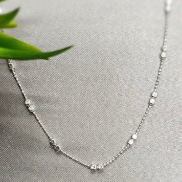 A sterling silver necklace with a square detail lying on a grey surface with a green leaf in the background.