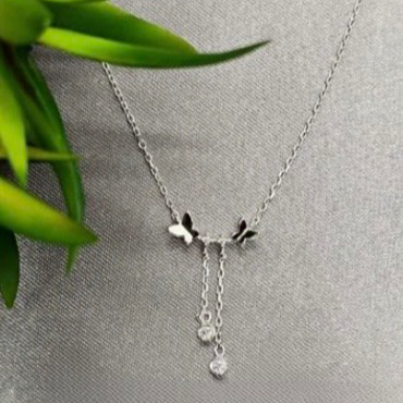 A sterling silver necklace with a butterfly-shaped pendant and dangling crystals displayed against a neutral background.