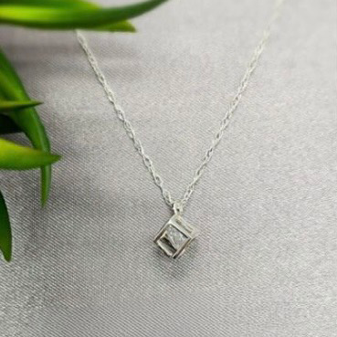 A sterling silver necklace with a clear cubic zirconia crystal pendant, displayed against a silver-toned background with a green leaf.