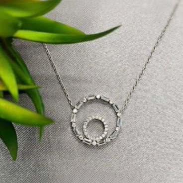 A sterling silver necklace with a double circle design embedded with cubic zirconia stones, displayed on a grey fabric.