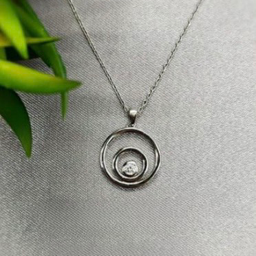 A sterling silver necklace with three circles and a cubic zirconia centre, displayed against a textured background with a green leaf.