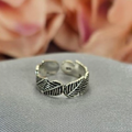 A sterling silver toe ring with a leaf pattern, displayed on a textured surface with a blurred background of pink flowers.