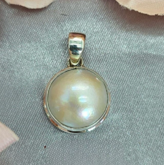 A 16mm white Mabe pearl pendant with a sterling silver cap and chain, displayed on a textured background.