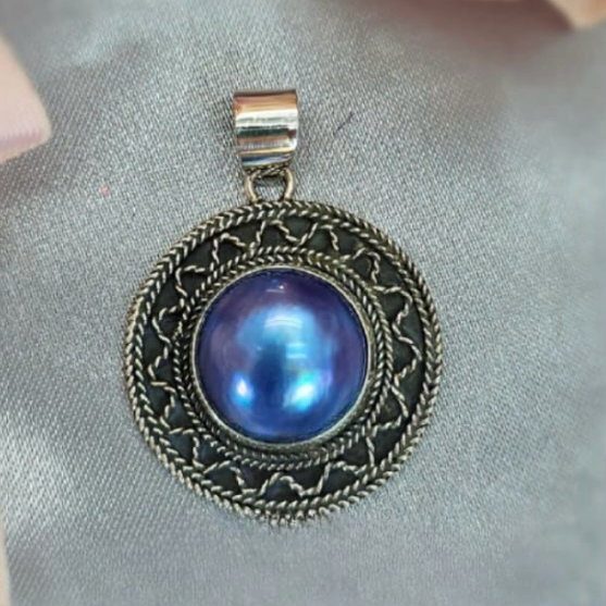 A sterling silver pendant featuring a blue Mabe pearl, displayed against a floral background.