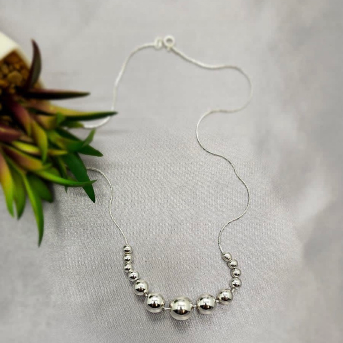 A sterling silver necklace with 13 silver balls, displayed against a white background with a floral accent.
