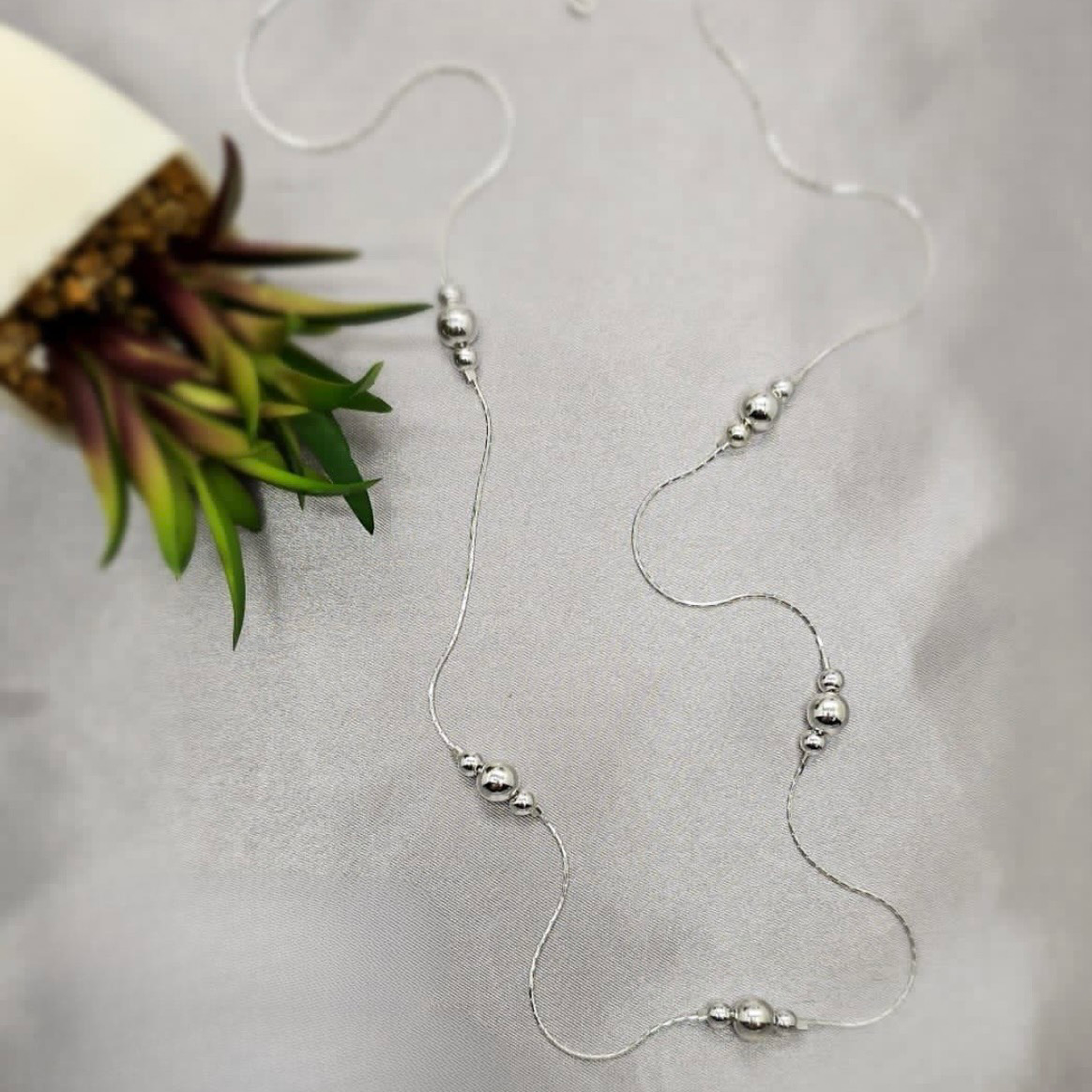 A 70cm sterling silver necklace with different sized ball details laid out on a textured surface.