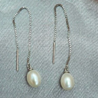 A pair of freshwater pearl shoe string earrings with silver hooks and thread detailing on a grey background.