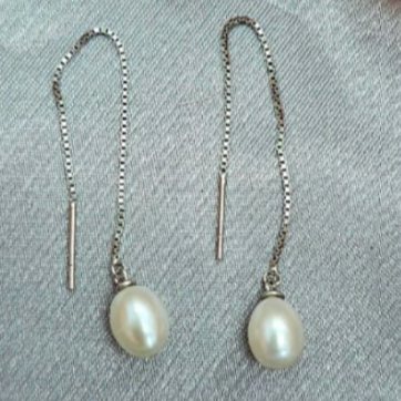 A pair of freshwater pearl shoe string earrings with silver hooks and thread detailing on a grey background.