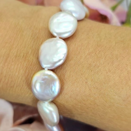 A person wearing a bracelet featuring blush pink coin pearls.