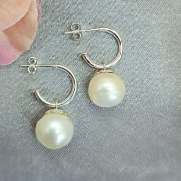 A pair of silver hoop earrings with flower-edged pearls on a textured background with pink flower petals scattered around.