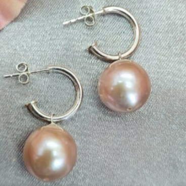 A pair of sterling silver hoop earrings with pink/brown freshwater pearls attached to them, displayed on a textured surface.