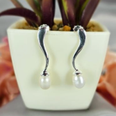 A pair of sterling silver drop earrings with freshwater pearls on the end, displayed against a plant backdrop.