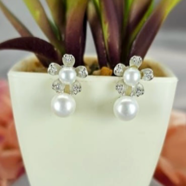 A pair of sterling silver earrings featuring freshwater pearl flowers, displayed in a white vase with green leaves.