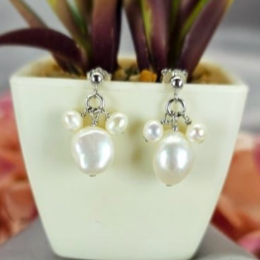 A pair of sterling silver drop earrings with three dangling pearls, displayed in a white vase with a green plant in the background.